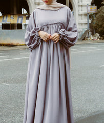 A woman wearing a modern mauve A-line abaya dress with a smocked bodice and ruffled sleeves from the latest abaya collection 2026.