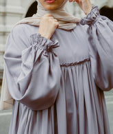 A woman wearing a modern mauve A-line abaya dress with a smocked bodice and ruffled sleeves from the latest abaya dresse collection 2026.