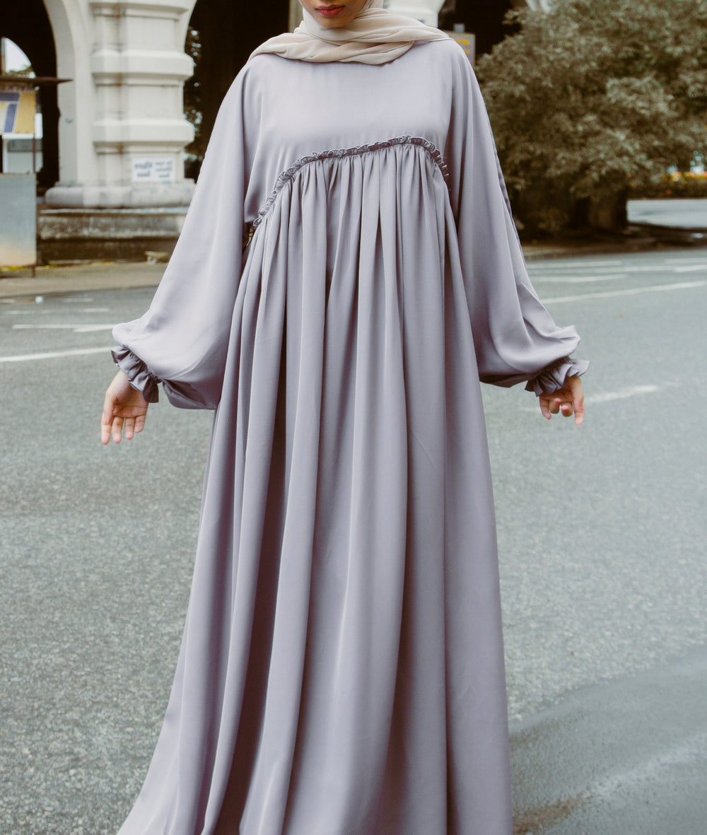 A woman wearing a modern an abaya dress with a smocked bodice and ruffled sleeves from the latest abaya shop dress collection 2026.