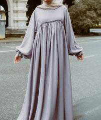 A woman wearing a modern an abaya dress with a smocked bodice and ruffled sleeves from the latest abaya shop dress collection 2026.