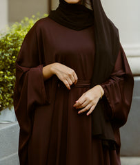 Woman wearing a chocolate brown wide-sleeve kaftan abaya dress with a waist belt, showcasing the latest abaya designs 2026 for a modern abaya collection.