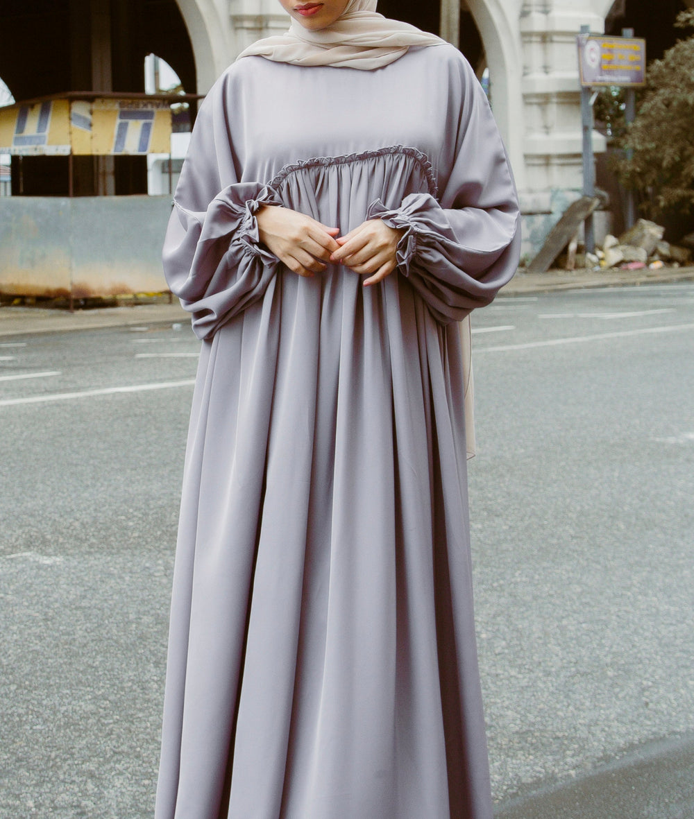 A woman wearing a modern mauve A-line abaya dress with a smocked bodice and ruffled sleeves from the latest abaya collection 2026.
