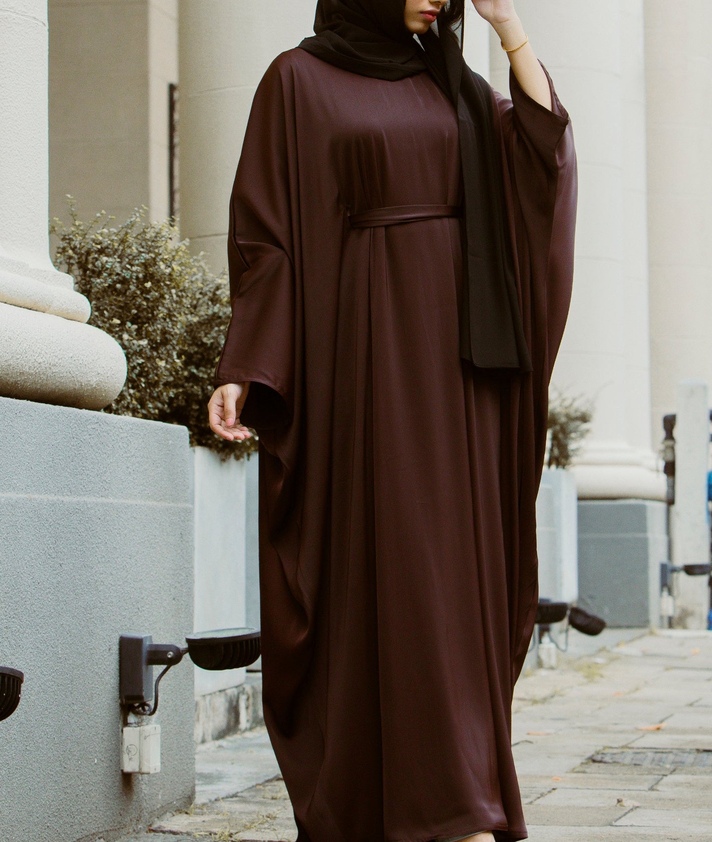 Woman wearing a chocolate brown wide-sleeve kaftan abaya dress with a waist belt, showcasing the latest abaya designs 2026 for a modern abaya collection.